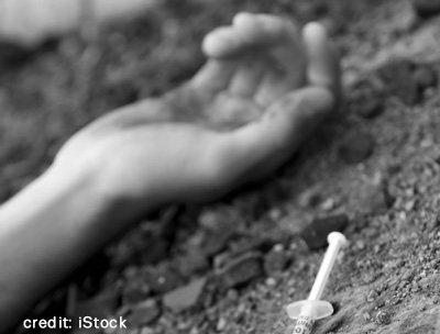 Picture of a hand on the ground with syringe in foreground